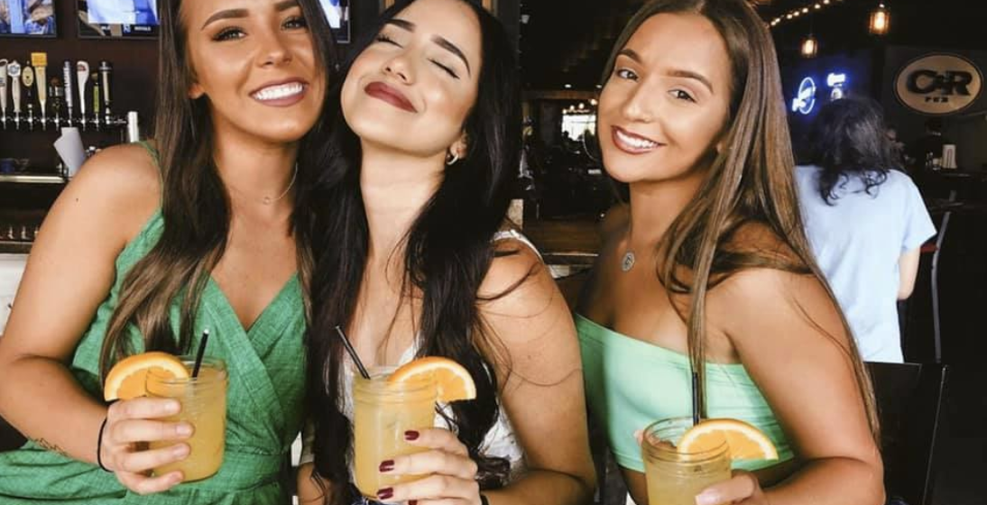 Three women are posing for a picture while holding drinks.