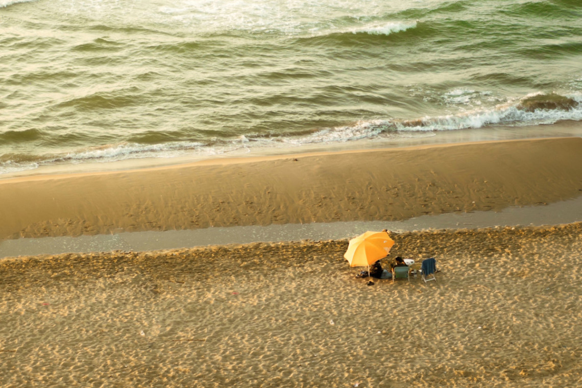 Two people sitting on a beach under an umbrella.