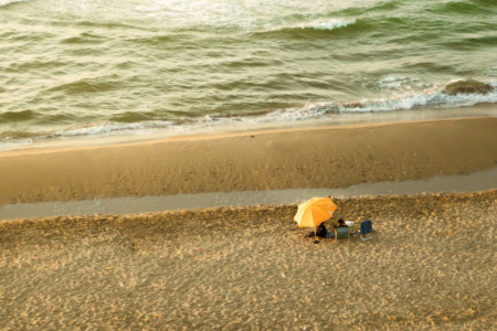 Two people sitting on a beach under an umbrella.