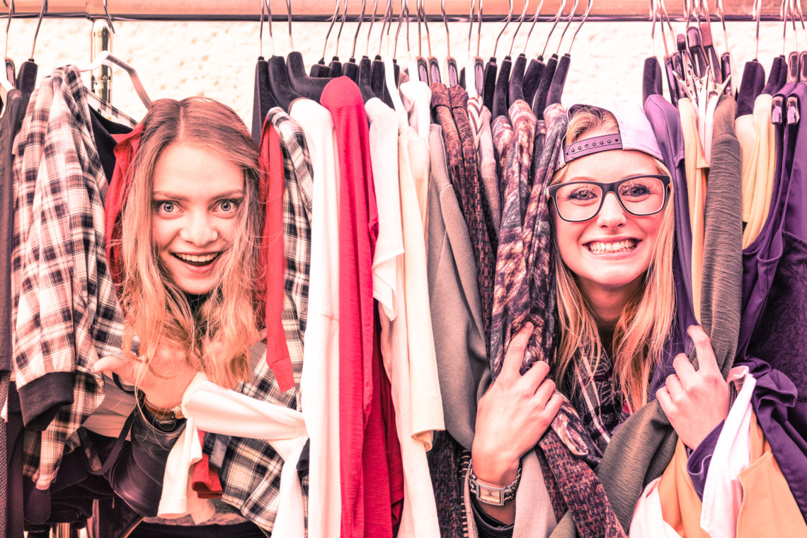 Two women browsing a rack of clothes at a flea market.